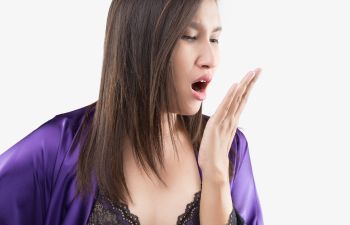 A woman in nightgown checking her breath.