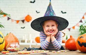 A little happy girl in a witch hat leaning over Halloween sweets.