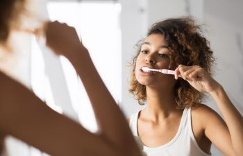 Afro-American woman brushing her teeth in front of the bathroom mirror.