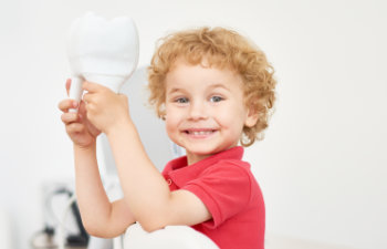 smiling boy in the dental office holding a big toy tooth, 