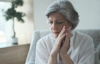 Elderly senior woman massaging her temples to reduce her headache. Older lady feeling scared, anxious, and thinking of sickness or mental health while suffering from a severe migraine or memory loss., 